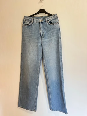 Ljusblåa raka jeans med hög midja från monki - Jeans från monki, storlek 26. Passar för personer med storlek S. Rak passform och hög midja. Jeansen har klassisk femficksdesign, bälteshällor och stängs med knapp och dragkedja. Materialet är denim i bomull och benen är långa och raka för en avslappnad look.