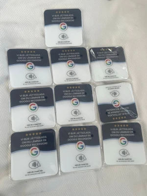 10st Google recension NFC-klistermärken - Säljer ett gäng fyrkantiga NFC-klistermärken i vitt och svart med Google-logga. Texten uppmanar till att lämna en Google-recension genom att hålla mobilen mot märket. Perfekt för företag som vill samla recensioner snabbt och smidigt.