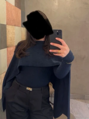 Mörkblå ponchotröja med polokrage - Snygg mörkblå ponchotröja med polokrage och vida ärmar. Tröjan har en unik cape-liknande design som ger en cool och trendig look. Perfekt att styla med höga byxor eller kjol för en modern outfit. Använts 2-3 gånger, skriv för fler bilder 