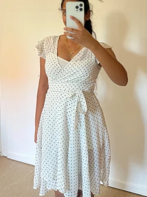 Vit omlottklänning med prickar från bikbok - Säljer en vit/cremefärgad omlottklänning från bikbok i storlek XS. Klänningar har svarta prickar, kort ärm, markerad midja och knytband. Priset kan sänkas vid snabb affär.   • Omlottmodell med V-ringning • Knytband i midjan som ger en fin siluett • Korta, lätt volangiga ärmar • Vid/fallande kjol • Vit/creme med svarta prickar • Storlek XS • Perfekt till vardag, sommar, semester, brunch eller fest 💕
