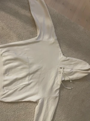Klassisk vit hoodie med ficka - En stilren vit hoodie med luva samt en stor magficka framtill. Tillverkad i mjukt material, perfekt för en avslappnad look. Ribbstickade muddar vid ärmslut och nederkant ger en snygg passform.