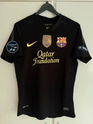 FC Barcelona 11/12 Borta Tröja - Barcelona Messi tröja från säsongen 2011/2012. Tröjan har även Champions League trycken på ärmarna samt FIFA Club World Cup tryck på bröstet. Storleken är M men skulle säga att den sitter mer som S. Tveka inte att höra av er för fler frågor och bilder!