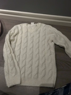 Vit kabelstickad tröja Time to Lounge - Kabelstickad vit tröja från Time to Lounge med rund halsringning och ribbade muddar. Tröjan har ett klassiskt flätmönster och är perfekt för dig som gillar en enkel men snygg look. Passar till många olika outfits och är supermysig.
