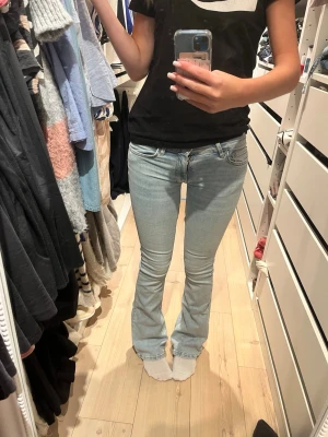 Ljusblå bootcut jeans - Säljer ett par ljusblå bootcut jeans med klassisk femficksdesign och låg midja. Jeansen har en snygg tvätt och är tillverkade i stretchigt denimtyg som sitter tajt över låren och släpper ut vid bensluten. Perfekta för en avslappnad och trendig look.