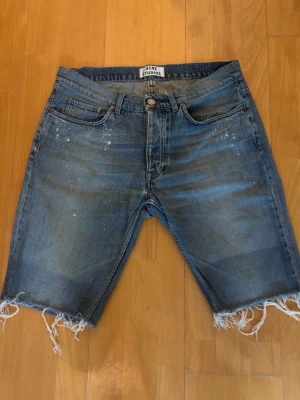 Blå jeansshorts från Acne Studios - Säljer ett par blå jeansshorts från Acne Studios med råa, fransiga benslut och slitna detaljer. W34. Shortsen är i ganska bra skick, hör av er vid funderingar🙌