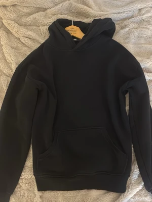 Svart hoodie från BikBok - En klassisk svart hoodie från BikBok i storlek XS. Hoodien har en stor huva, magficka och ribbade muddar vid ärmslut och nederkant. Tillverkad i mjukt och bekvämt material, perfekt för en avslappnad stil.