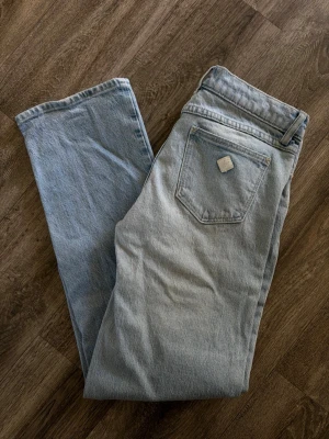 ABRAND JEANS  - Säljer ett par ljusblå jeans med rak passform och fem fickor. Jeansen har en klassisk look med hög midja och detaljer i kopparfärg vid fickorna. Materialet är denim i bomull och färgen är snyggt tvättad för en vintagekänsla. Storlek 27/AU 9