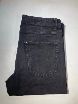 Svarta raka jeans - Säljer ett par svarta jeans med rak passform och klassisk femficksdesign. Jeansen har bälteshällor och knappgylf. Materialet är denim i bomull och de har en stilren look som funkar till det mesta.