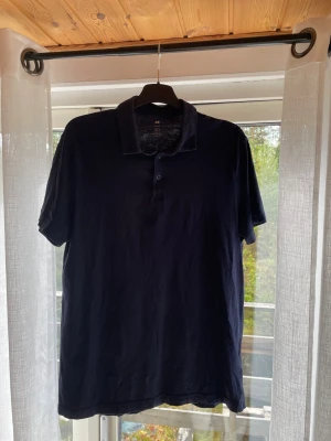 Mörkblå slim fit piké från H&M - Säljer en mörkblå pikétröja från H&M i slim fit-modell. Skjortan har korta ärmar, klassisk krage och knappar framtill. Perfekt för en clean och enkel stil.