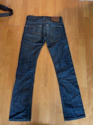 Blå jeans från Lee med raka ben - Säljer ett par klassiska blå jeans från Lee med raka ben och kontrastsömmar. Jeansen är från Lee’s 120th anniversary 2009. Sitter mer åt det slimma hållet samt är bootcut. Hör av er vid funderingar. W29 L32
