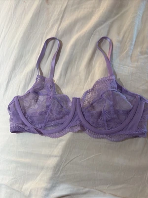  spets-bh  - Säljer en lila bh från Hunkemöller i transparent spets med bygel och justerbara axelband. Bh:n har en feminin design med tunna band och vacker spetsdetalj. Perfekt för dig som gillar en romantisk och trendig look.