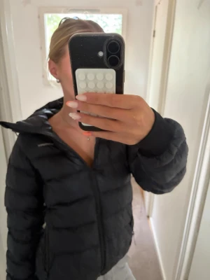 Svart pufferjacka med huva - Säljer en svart pufferjacka med dragkedja och huva. Jackan har en klassisk quiltad design och är perfekt för kalla dagar. Den är lätt vadderad och har en stilren look som passar till det mesta. Jackan har resår vid ärmsluten för extra komfort.jackan har oxå ett hår vid armen men inget man lägger märke till o går att fixa💕