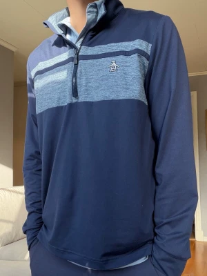 Original Penguin golftröja 1/4 zip – blå - Snygg golftröja från Original Penguin i mörkblått med melerad ljusblå panel över bröstet. Klassisk 1/4-zip med hög krage och broderad Penguin-logga på bröstet.  Sportig och stilren modell som passar perfekt för golf eller vardag. Fint begagnat skick med normalt, lätt slitage.  