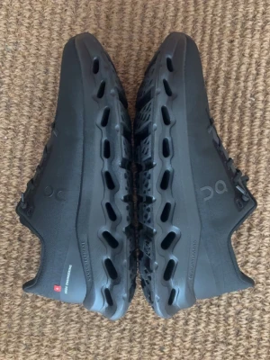 Svarta On Cloud Skor  - Säljer ett par svarta On Cloudnova sneakers med unik sula och ventilerande meshmaterial. Skorna har lågt skaft, snörning och diskret logga på sidan. Perfekta för dig som gillar stilrena och futuristiska sneakers med grym komfort.