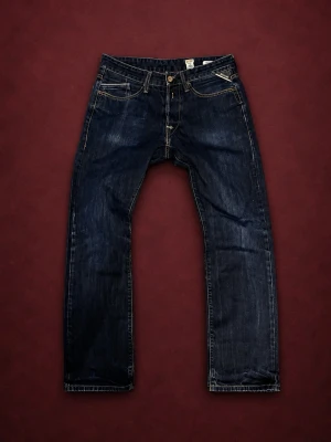 Mörkblå jenas från Replay - Säljer ett par mörkblå jeans från Replay med raka ben och klassiska kontrastsömmar. Jeansen har fem fickor och gylf med knapp och dragkedja. Materialet är slitstark denim och passformen är avslappnad. Perfekt för dig som gillar en tidlös look.