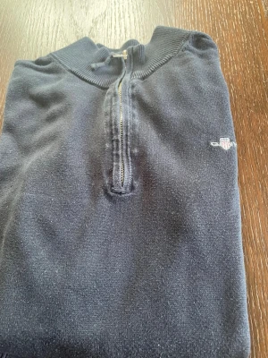 Mörkblå halvzip tröja - Snygg mörkblå tröja med halv dragkedja och ribbade muddar. Liten broderad logga på bröstet. Perfekt till jeans eller chinos för en clean look. Materialet känns mjukt och bekvämt, och tröjan har en klassisk passform med hög krage.
