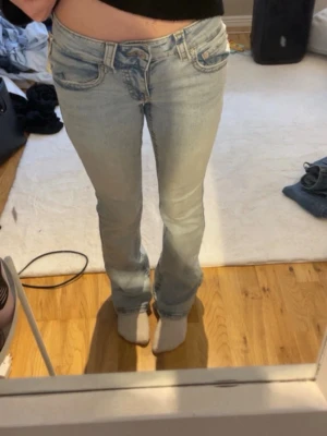Ljusblå bootcut jeans med fickdetaljer - Säljer ett par ljusblå bootcut jeans med snygga fickdetaljer både fram och bak. Jeansen har klassisk femficksdesign, bälteshällor och en avslappnad passform. Perfekta till en casual look och tillverkade i denim med lätt tvättad effekt.