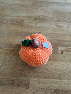 Virkad orange pumpa  - Handgjord pumpa i orange, virkat av mjukt och fluffigt garn. Dekorerad med ett brunt skaft och grönt blad på toppen. Perfekt som höstdekoration eller till halloween. Söt och unik inredningsdetalj som passar på bord eller hylla.