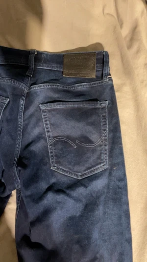 Mörkblå slim fit jeans - Säljer ett par mörkblå slim fit jeans med klassisk femficksdesign och snygga sömdetaljer på bakfickorna. Jeansen har bälteshällor, knappgylf och är tillverkade i ett mjukt denimtyg som ger en skön passform.