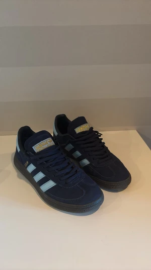 Adidas Spezial  - Säljer ett par Adidas Originals Samba OG sneakers i marinblått med ljusblå detaljer och klassiska vita stripes. Skorna är i mycket fint skick, knappt använda och ser nästan nya ut. Perfekta till både vardag och fritid! Köp direkt eller skicka prisförslag.