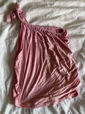 Rosa oneshoulder topp från Calliope - Säljer en ljusrosa oneshoulder topp från Calliope. Toppen har ett axelband som knyts och är gjord i mjuk bomull. Är o ONE SIZE då bandet går att justera. Dock lite pösig på mig som är vanligtvis XS/S