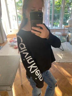 Svart tröja från Calvin Klein - Jättesnygg svart tröja från Clavin Klein med vitt tryck på ena armen. Superenkel att styla med ett par jeans eller kjol och funkar i all årstider. Jag säljer den nu så den inte är min stil längte😊🥰