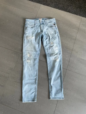 Replay Anbass - Säljer ett par ljusblå skinny jeans med slitningar och distressed detaljer på framsidan. Jeansen har klassisk femficksmodell och raka ben. Perfekta för en avslappnad och trendig look.