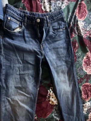 Mörkblå raka jeans - Säljer ett par mörkblå jeans med raka ben och klassisk femficksmodell. Jeansen har slitningar och ljusare partier framtill för en trendig look. Passar perfekt till en avslappnad stil.