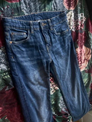 Blå raka jeans med slitningar - Säljer ett par klassiska blå jeans med raka ben och lätt slitna detaljer. Jeansen har fem fickor, normal midja och kontrastsömmar. Perfekta för en avslappnad och trendig look.