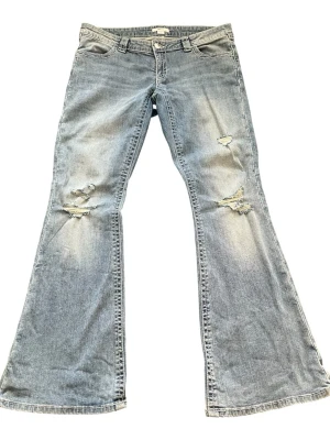 Gina tricot Ljusblå bootcut jeans med brodyr - Säljer ett par ljusblå bootcut jeans med slitningar och hål på framsidan. Baktill har fickorna snygg brodyr i beige. Använd typ 2 gånger