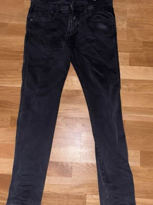 Svarta slim fit jeans - Säljer ett par svarta slim fit jeans från Replay med klassisk femficksdesign och diskreta sömmar. Jeansen har normal midja och dragkedja med knapp. Materialet är mjukt och stretchigt för extra komfort. De 2 sista bilderna så ser man att de finns några hål som är ganska synliga men går att fixa hos en skräddare eller genom att sy själv 