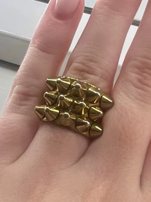 Edblad guldig ring med nitar - Edblad ring i guldfärgad metall med flera rader av konformade nitar. Börjar tappat lite färg men ingen som syns om man bara har den på fingret