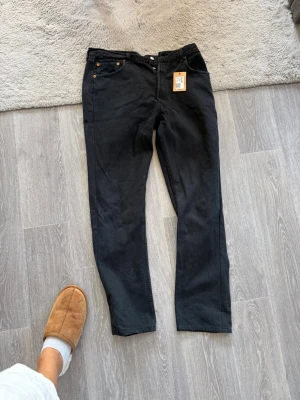Svarta raka jeans - Säljer ett par svarta jeans med rak passform och klassisk femficksdesign. Jeansen har knappgylf och är tillverkade i ett mjukt denimtyg. Perfekta för en clean och stilren look.