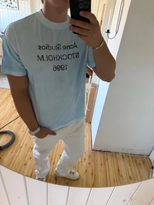 Ljusblå Acne Studios t-shirt - Säljer en ljusblå t-shirt från Acne Studios med tryck på bröstet där det står 'Acne Studios STOCKHOLM 1996'. T-shirten har en klassisk passform och är kortärmad. Perfekt för dig som gillar stilrena och trendiga plagg. Storlek L utmärkt skick