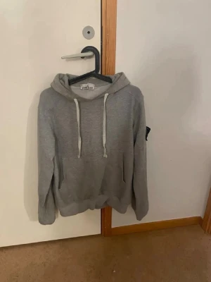 Grå hoodie med huva och ficka - Säljer en enkel och stilren grå hoodie med huva och vita dragsnören. Hoodien har en stor magficka framtill och ribbade muddar vid ärmslut och nederkant. Perfekt för en avslappnad och casual look.