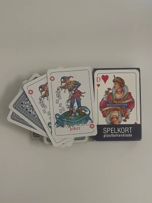 Spelkort plastbehandlade klassiska - Kortlek med plastbehandlade spelkort i klassisk design. Korten har färgglada illustrationer som joker och dam i hjärter, samt blåvitt mönster på baksidan. Perfekt för olika kortspel och pokerkvällar.