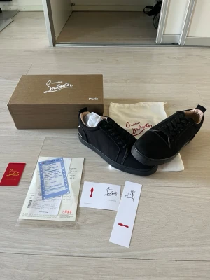 Svarta sneakers från Christian Louboutin - Snygga svarta sneakers från Christian Louboutin med vit signatur på hälen och svarta skosnören. Skorna har en stilren design med låg profil och är tillverkade i slätt läder. Perfekta för dig som vill ha en exklusiv och trendig look.