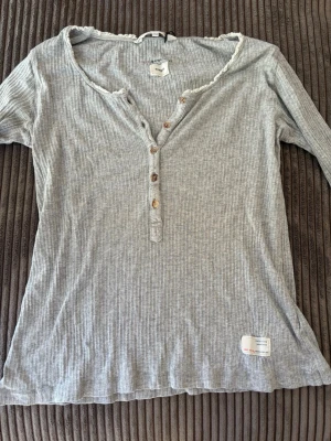 Grå ribbad trekvarts ärmad topp Odd Molly - Grå ribbad trekvarts ärmad topp från Odd Molly med v-ringning och dekorativa knappar framtill. Toppen har en lätt vågig kant vid halsen och en liten tygpatch med text nedtill. Skickar inom 1-2dagar!💓