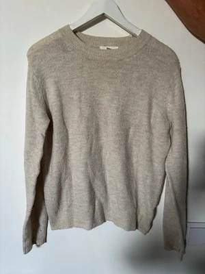 Beige stickad tröja  - Mysig beige stickad tröja med rund hals och långa ärmar. Tröjan har en enkel och stilren design med ribbstickade muddar vid ärmslut och nederkant. Perfekt för lager på lager och passar till det mesta. Materialet känns mjukt och värmande.