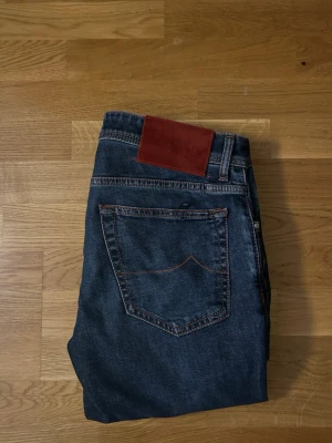 Jacob Cohen jeans  - Snygga mörkblå jeans med raka ben och klassisk femficksdesign. Jeansen har kontrastsömmar i orange och en röd patch bak i midjan. Perfekta för en avslappnad och trendig look. W33 garn, näsduk och lapp hänger med. 
