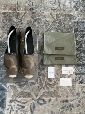 Valentino Kamouflagefärgade espadrillos  - Snygga espadrillos från Valentino i kamouflagemönster. Skorna har en klassisk slip-on design med canvasmaterial och flätad sula i naturfärg. Perfekta för dig som vill sticka ut med en trendig och avslappnad stil.