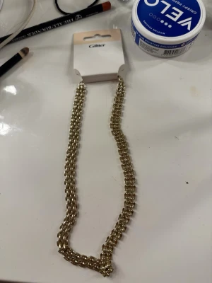 Guldigt halsband från Glitter - Snyggt halsband i guldfärgad metall från Glitter. Halsbandet har en kedja med små pärlliknande detaljer som ger ett trendigt och elegant intryck. 