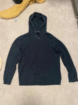 Mörkblå hoodie från J.Lindeberg - Snygg mörkblå hoodie från J.Lindeberg med broderad logga på bröstet. Klassisk modell med huva och dragsnören samt stor magficka framtill. Tillverkad i mjuk bomull för skön känsla och avslappnad stil.