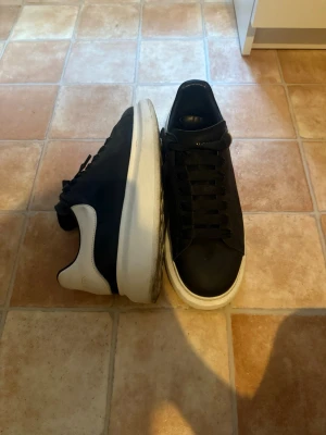 Två par sneakers i svart och grått - Säljer två par sneakers. Ett par är svarta med vit sula och detaljer, klassisk låg modell med slät ovandel och svarta skosnören. Det andra paret är gråa med mesh-ovandel, vita och mörkgrå detaljer samt vita snören. Båda paren har chunky sulor och sportig look.