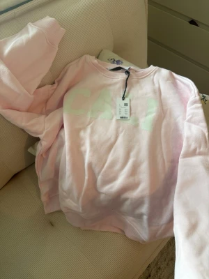 Ljusrosa sweatshirt med text - Säljer en ljusrosa sweatshirt med vit text 'CALI' framtill. 