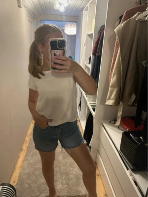 Blå denimshorts med rå kant - Säljer ett par klassiska blå denimshorts med rå, fransad kant. Shortsen har hög midja och normal passform, perfekta för sommaren. Tillverkade i bomull för en skön och avslappnad känsla.