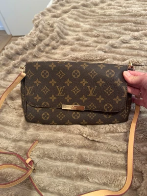 Brun axelväska - Snygg axelväska i brunt. Väskan har en lång justerbar axelrem i ljust läder och ett innerfack. Perfekt för dig som vill ha en ikonisk och stilren accessoar.