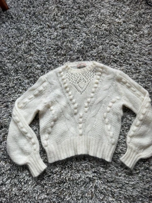 Vit stickad tröja med strukturmönster - Säljer en krämvit stickad tröja med snyggt strukturmönster och virkade detaljer framtill. Tröjan har ballongärmar och bred ribbad mudd vid ärmslut och nederkant. Tröjan är från Twinset Milano och har nypris på ~2500