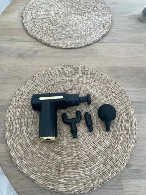 Svart massagepistol med tillbehör - Säljer en svart massagepistol med gulddetaljer och tre olika massagehuvuden. Perfekt för att mjuka upp muskler och slappna av efter träning eller en lång dag. Kompakt design och enkel att använda, laddas via USB.