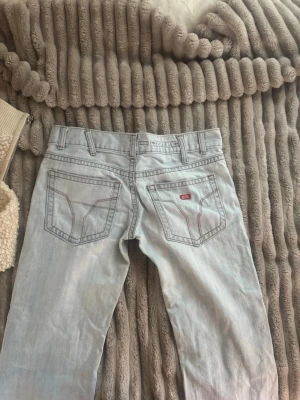 Ljusblå raka jeans från Levi's - Säljer ett par ljusblå jeans från Levi's med raka ben och klassiska bakfickor med kontrastsömmar. Jeansen har fem fickor, bälteshällor och en liten röd Levi's-lapp på ena bakfickan. Perfekta för en avslappnad och trendig look.